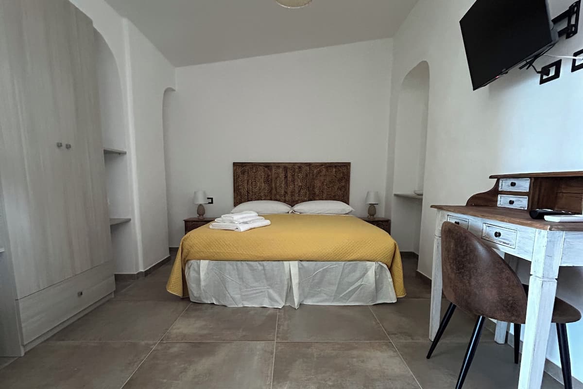 A bedroom with a bed, bedside tables, a desk, and a television.