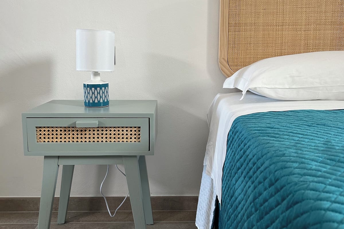 A neatly arranged bedroom with a bed, a bedside table with a lamp, and a woven headboard.