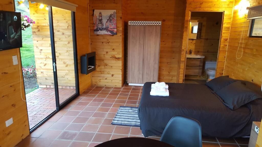 Quarto de madeira com cama, televisão, porta deslizante para um jardim e banheiro.