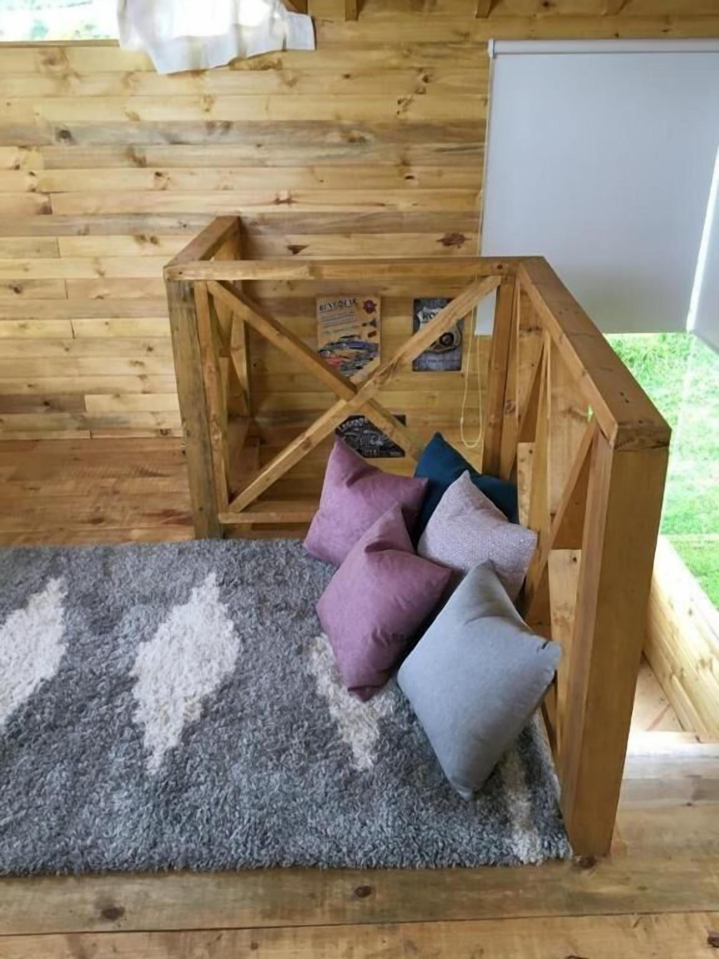 A wooden interior with a geometric wooden structure, a grey patterned rug, and several cushions.