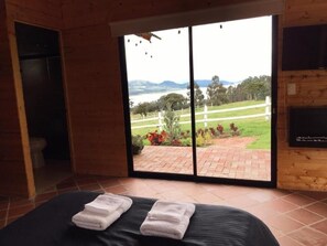 A room with a bed, a sliding glass door leading to a patio with a view of a landscape and a body of water. - Altozano Cabañas (Guatavita)