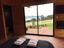 Una habitación con cama, una puerta corrediza de vidrio que da a un patio con vistas a un paisaje y un cuerpo de agua.