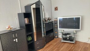 A modern living room with a dark wooden cabinet, a mirrored wardrobe, a flat-screen TV on a stand, and a glass coffee table. - 5 Minuten von Frankfurt, Ruhige Ferienwohnung/ Monteurzimmer mit Terrasse (Bad Vilbel)