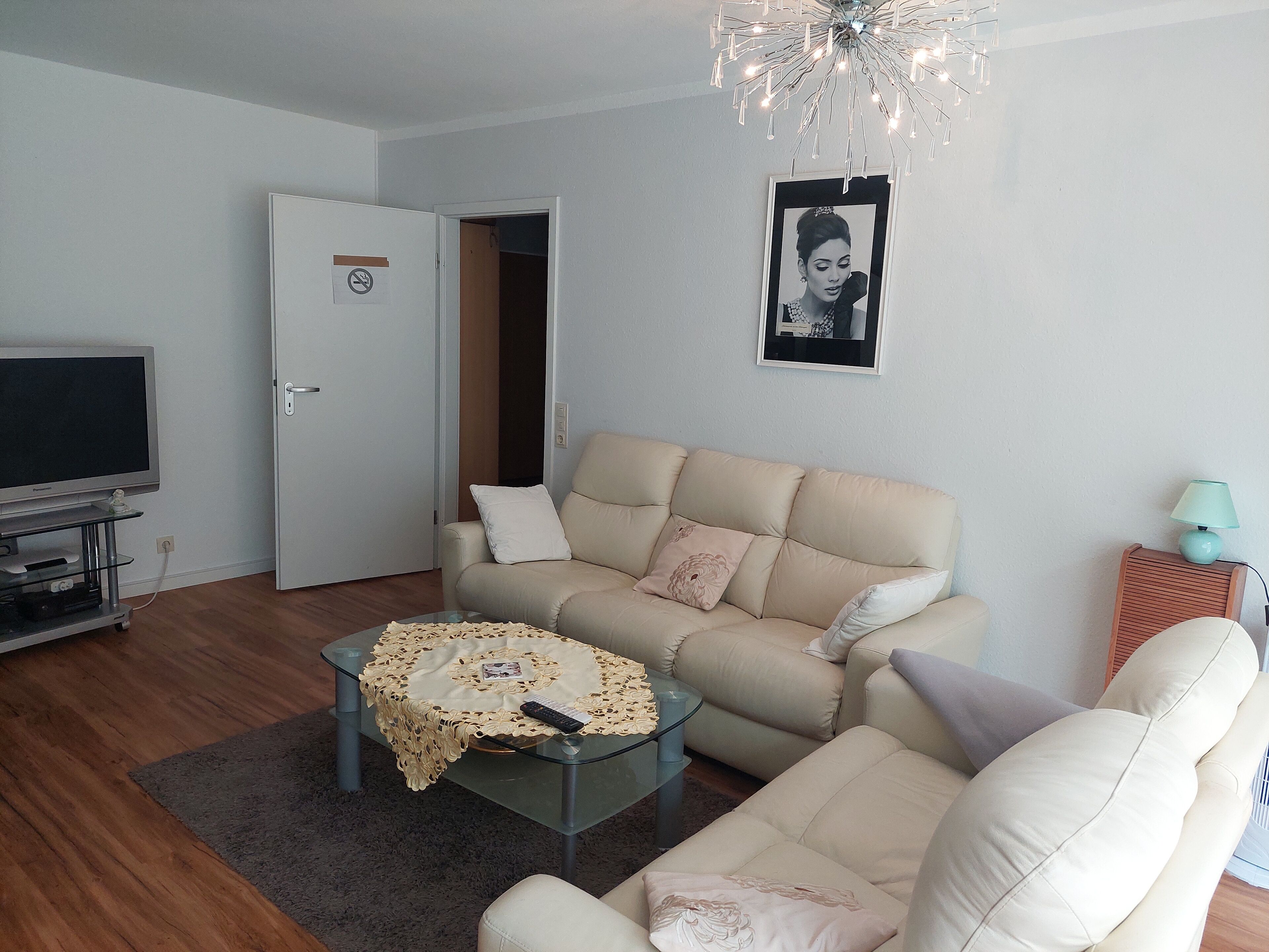 A living room with a sofa, a glass coffee table, a television, and a door.
