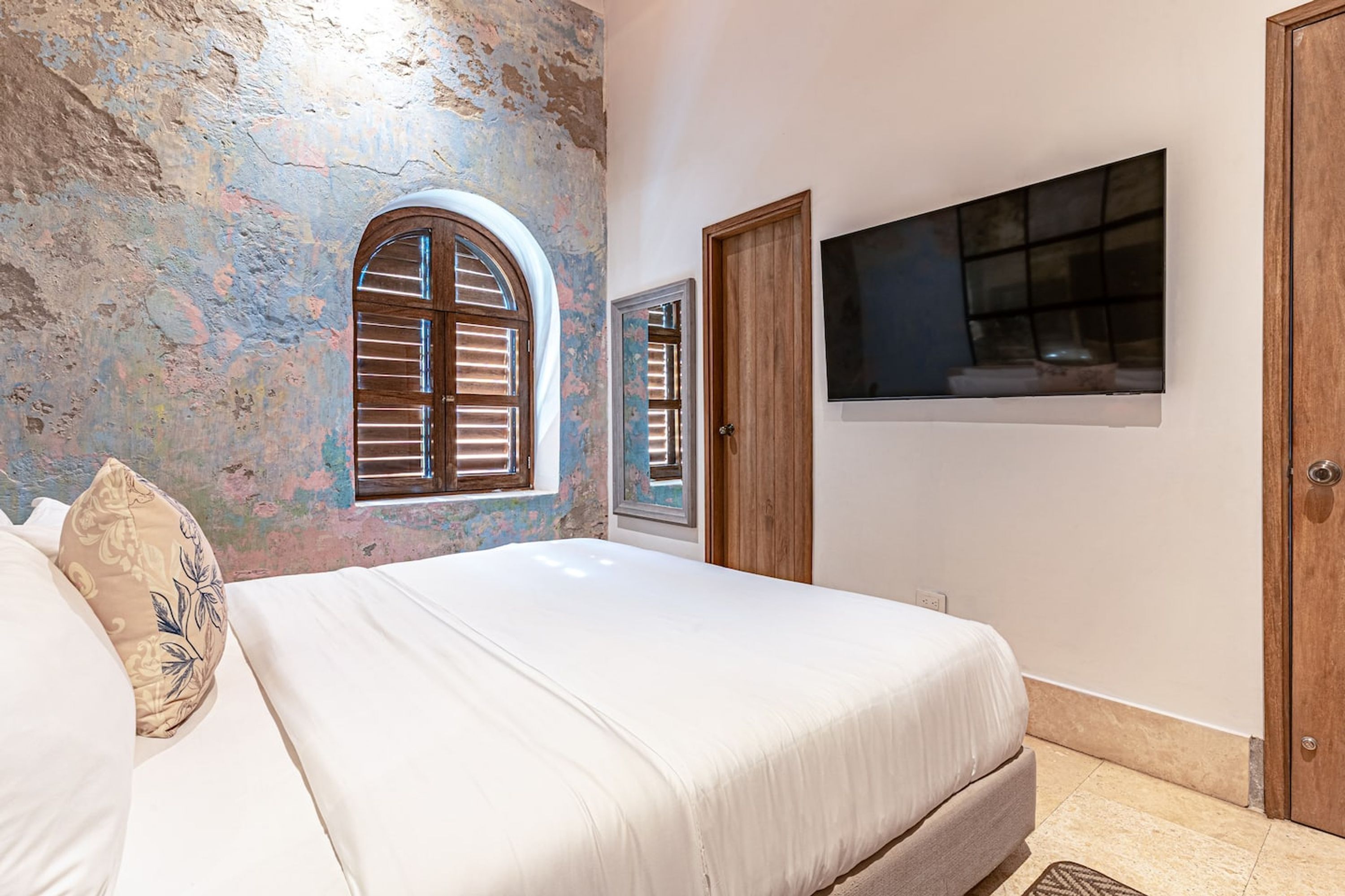 Een slaapkamer met een bed, een raam, een deur en een aan de muur bevestigde televisie.