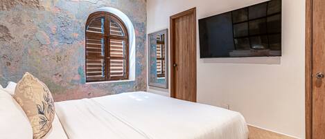 Een slaapkamer met een bed, een raam, een deur en een aan de muur bevestigde televisie.