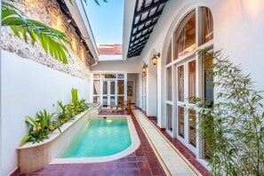 A pool area with a tiled floor, a stone wall, and potted plants. - Casa Torno - Piano Pool House (Cartagena)