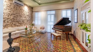 Een woonkamer met een vleugelpiano, een bank, een glazen salontafel en vloerbedekking met een patroon.