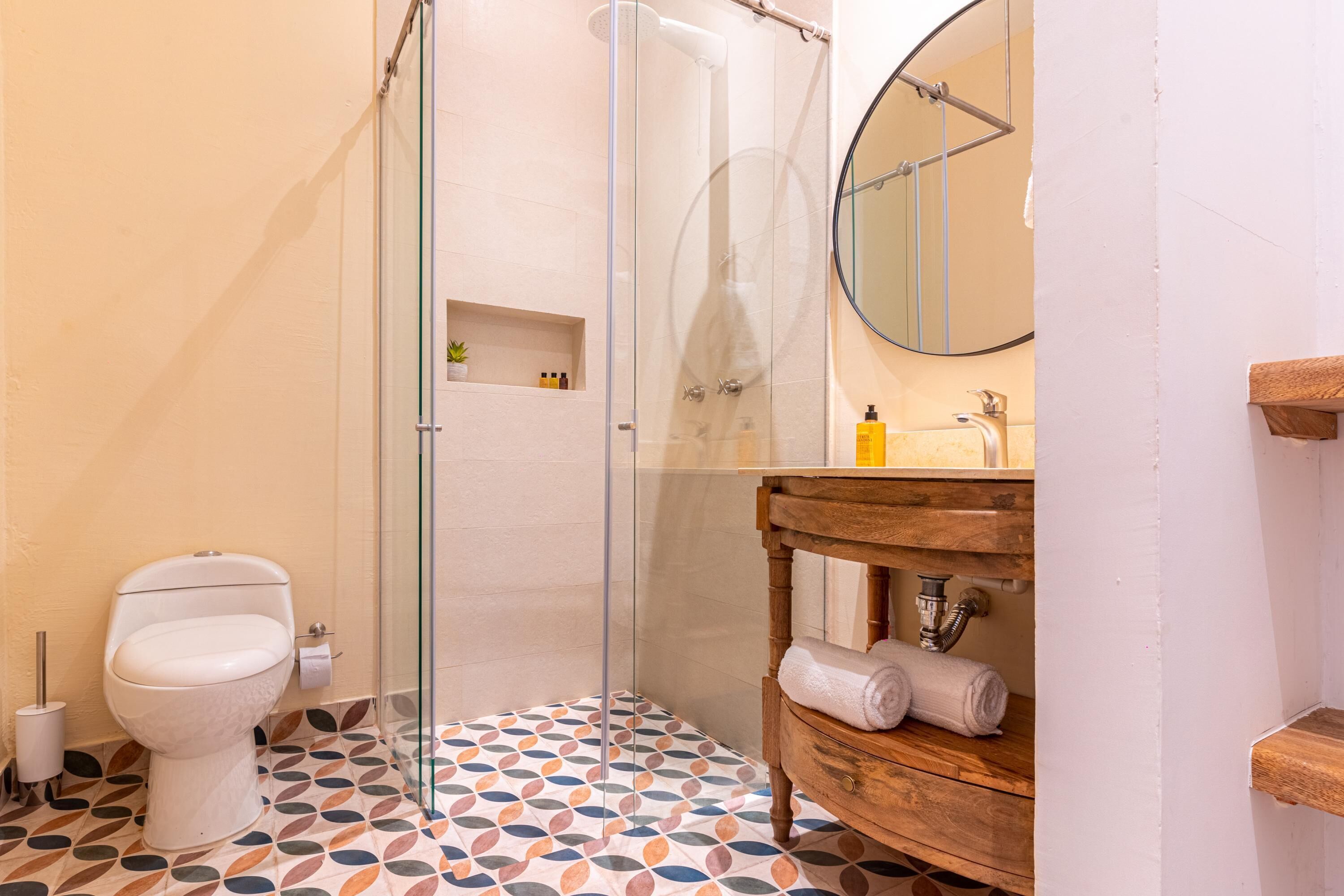 Une salle de bain comprenant des toilettes, une douche à parois de verre, un meuble-lavabo en bois et un miroir.
