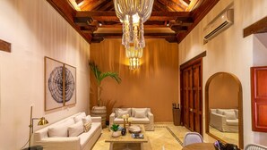A spacious living room with a high ceiling, a chandelier, a sofa set, a coffee table, and a dining table. - Casa Amande - Luxury House (Cartagena)