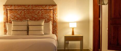 A neatly made bed with a patterned headboard, a bedside table with a lamp, and a wooden door with a metal handle.