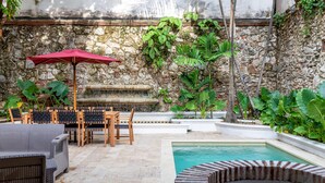 A pool area with stone walls, wooden furniture, and lush greenery. - Casa Amande - Luxury House (Cartagena)