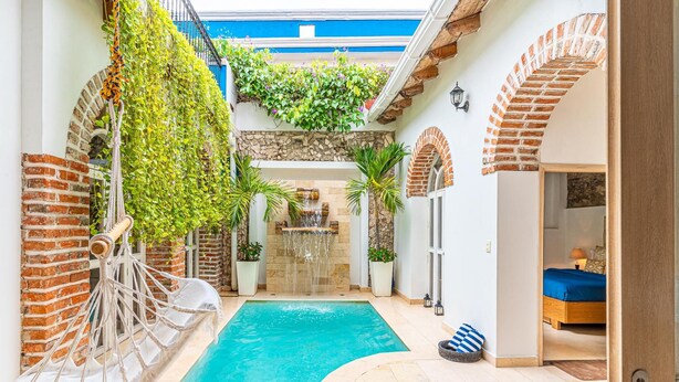 Zona de piscina con una hamaca, un muro de ladrillo y un muro de piedra con cascada.