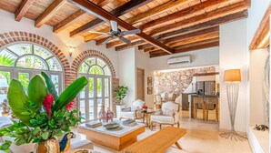 Amplia sala de estar con techo de madera, un ventanal con vistas a la naturaleza, un comedor con candelabro y una cocina al fondo.