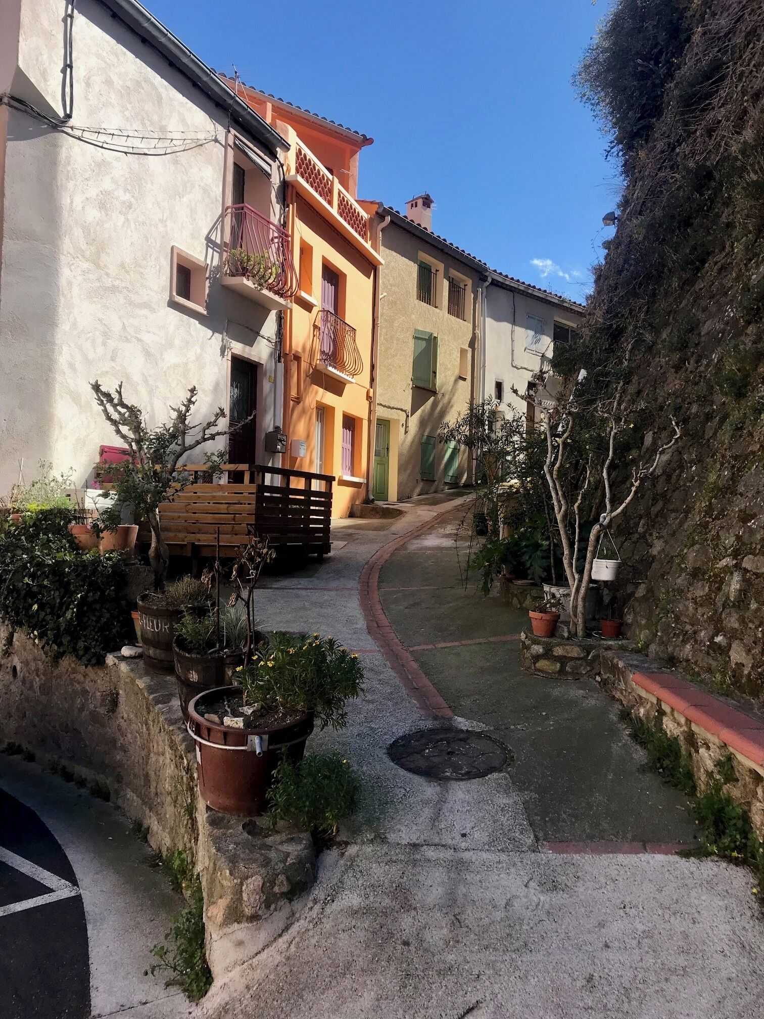 A narrow alleyway with buildings on either side, potted plants, and a wooden bench.