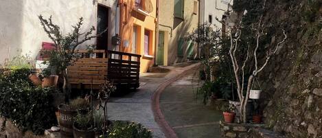 A narrow alleyway with buildings on either side, potted plants, and a wooden bench.