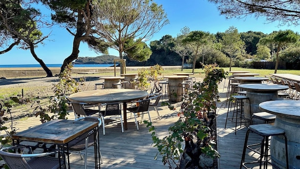 An outdoor patio with wooden tables and chairs, surrounded by trees and a view of the sea. - Vrbo Property
(Laroque-des-Albères)