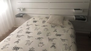 Un lit bien fait, recouvert d’une couvre-lit à motifs, une table de chevet avec une tasse, et un meuble à tiroirs placé sous le lit.