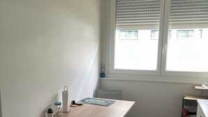 Une petite pièce lumineuse, avec une table en bois, deux chaises, un banc et une fenêtre équipée de stores.