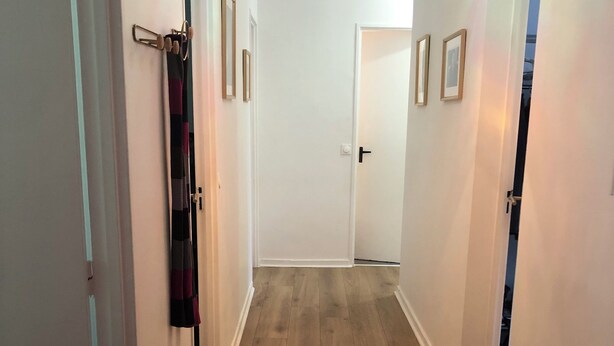 Un couloir doté d’un plancher en bois, de murs blancs et d’un luminaire au plafond.