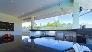 Une cuisine moderne dotée d’un grand îlot central, d’appareils électroménagers en acier inoxydable et offrant une vue sur la verdure environnante.