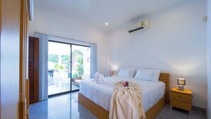 Une chambre d’hôtel équipée d’un lit, d’une table de chevet, d’un climatiseur et d’une porte-fenêtre coulissante donnant sur un espace extérieur.