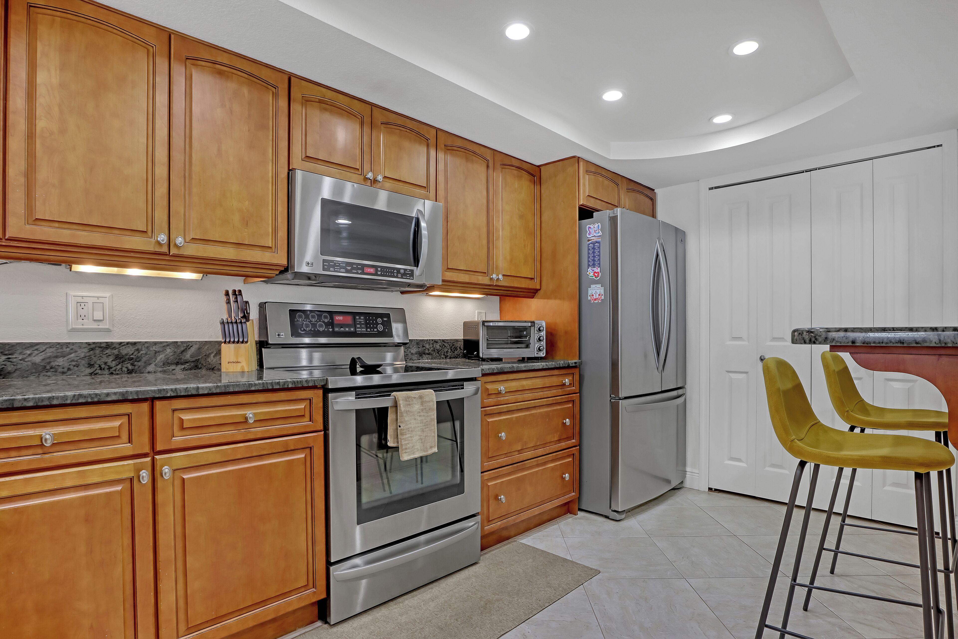 A modern kitchen with wooden cabinets, stainless steel appliances, and a marble countertop.