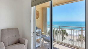 Un balcón con vista a la playa, una silla y una pequeña mesa.