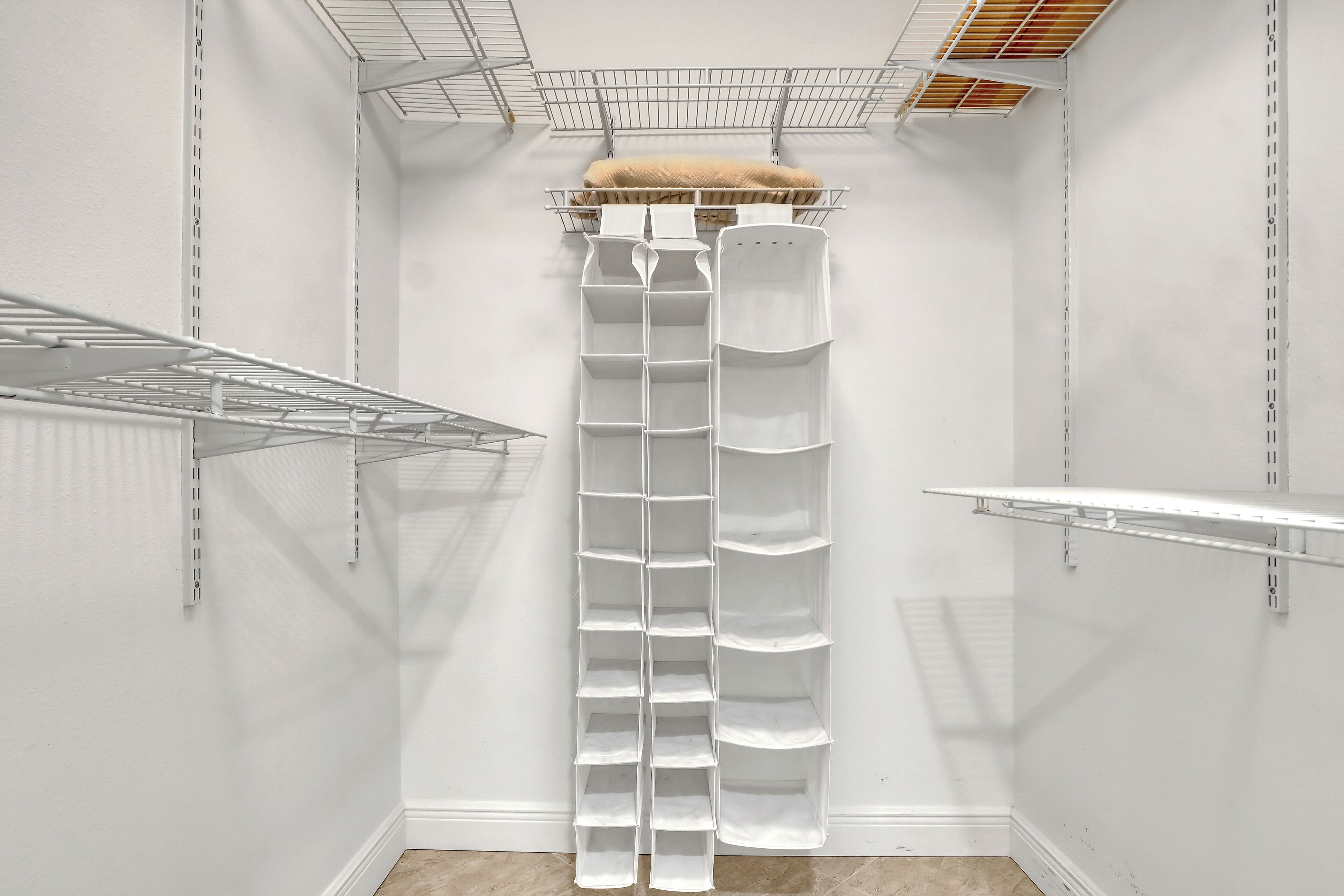 A white closet with multiple shelves and hanging space, a metal rack, and a fur coat on the top shelf.