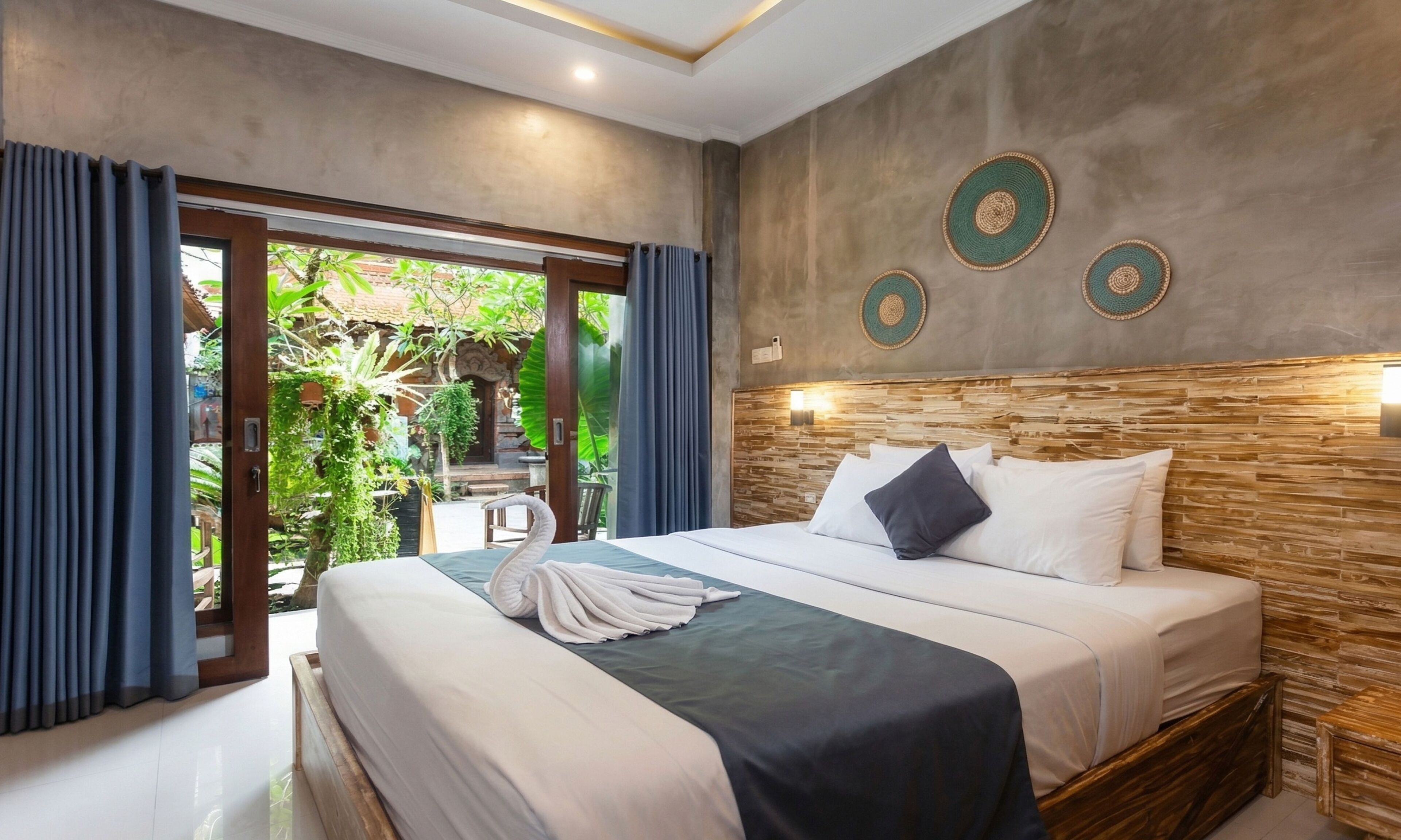 A bedroom with a bed, a wooden headboard, and a view of greenery outside.