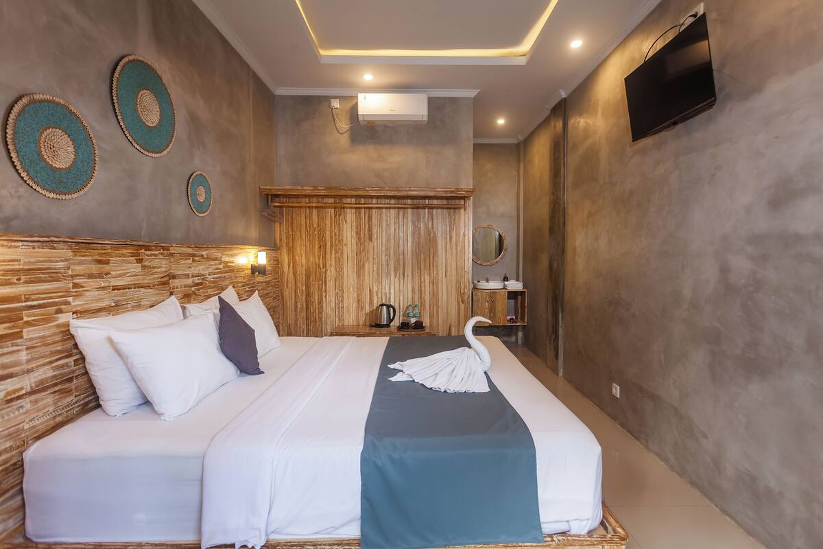 Une chambre d’hôtel moderne avec une tête de lit en bois, un lit recouvert de draps blancs, un plaid turquoise et un oreiller en forme de cygne.