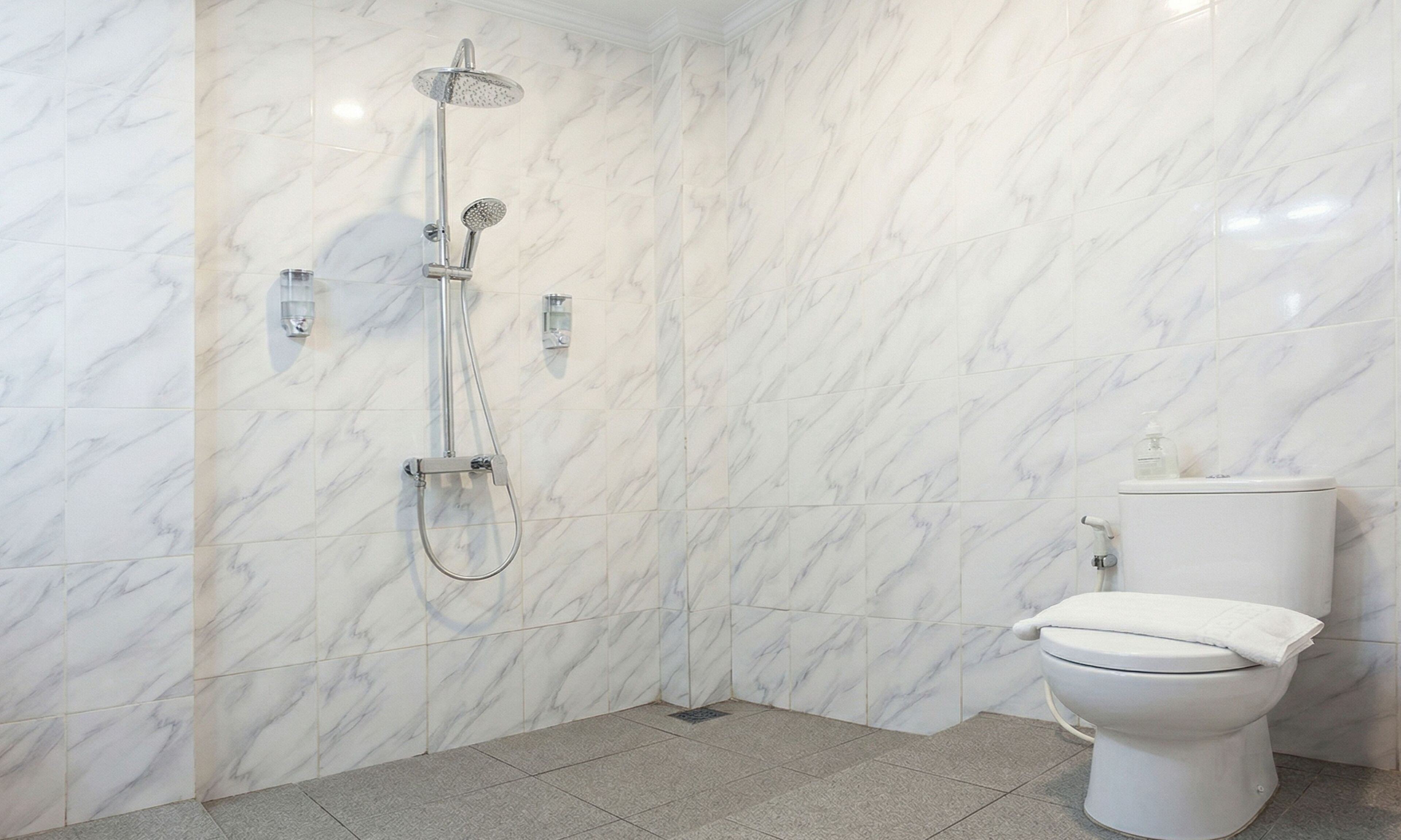Een badkamer met een douche, toilet en marmeren wanden.