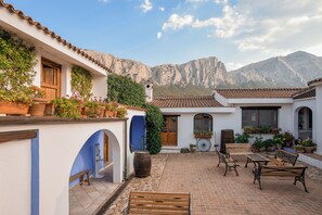 A courtyard with a brick floor, wooden benches, and potted plants. - Agriturismo Guthiddai (Oliena)