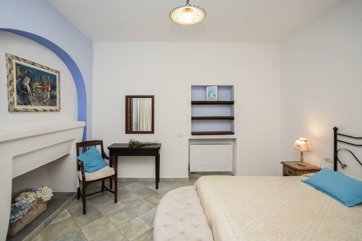 Un dormitorio con cama, una silla, un escritorio, un estante y una chimenea.