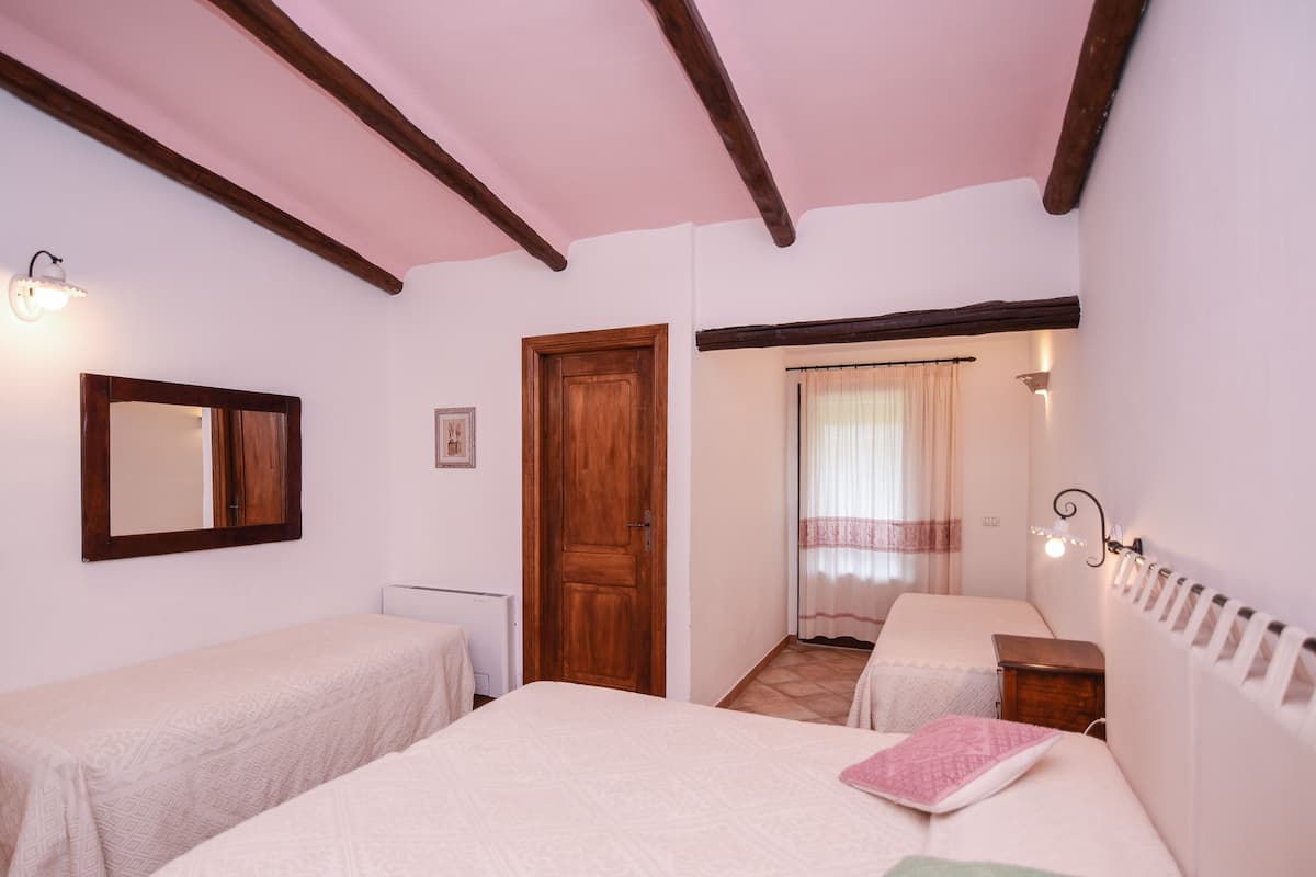 Un dormitorio con dos camas individuales, una puerta de madera, una ventana con cortinas y un radiador.