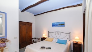 Quarto com cama, mesa de cabeceira, guarda-roupa de madeira, um quadro e uma janela.