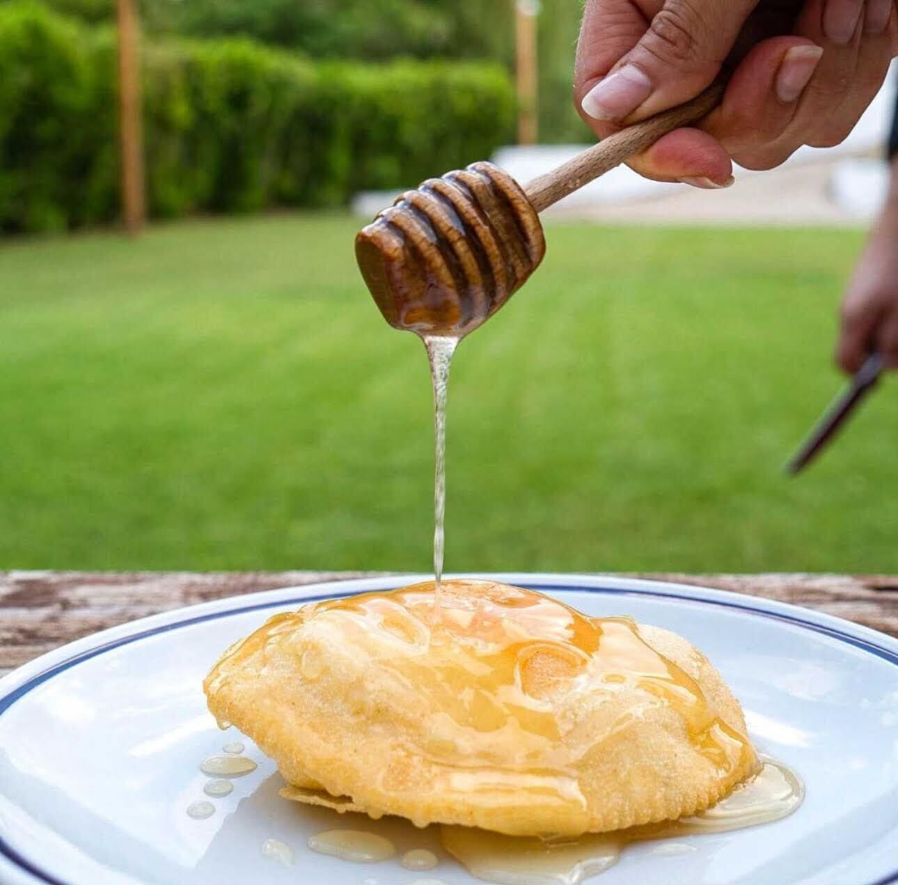 Een hand houdt een honinglepel vast, waar honing van druppelt op een bord met een gebakje.