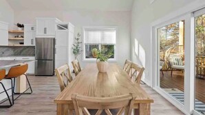 A modern kitchen with white cabinets, a stainless steel refrigerator, and a wooden dining table with chairs. - Jewel of the Hidden Cove (Littleton)