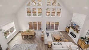 A spacious loft-style living area with a high ceiling, large windows, a fireplace, and a cozy seating arrangement. - Jewel of the Hidden Cove (Littleton)
