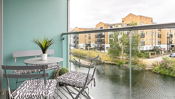 Ein Balkon mit Tisch und Stühlen, einem Blumentopf und Blick auf einen Kanal und Gebäude.