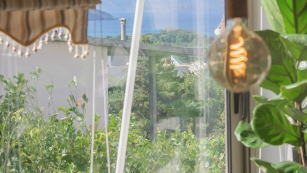 Ein Fenster mit Blick auf Grünflächen und Berge, ein Vorhang und eine Pendelleuchte.