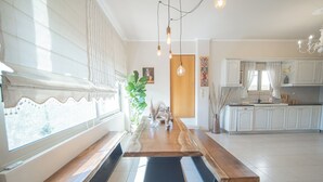 Eine moderne Küche mit Esstisch aus Holz, weißen Schränken und einem großen Fenster mit Jalousien.