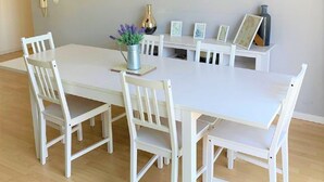 Un comedor con una mesa y sillas blancas, un florero con flores y un cuadro en la pared.
