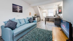 A modern living room with a blue sofa, a TV, and a kitchen in the background. - Liverpool Harrow Road Sleeps 6- Infinity Apartment (Liverpool)