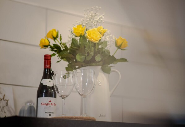 Una botella de vino, dos copas de vino y un florero con rosas amarillas sobre una encimera de cocina.