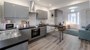 A modern kitchen with a central island, built-in appliances, and a dining area with a table and chairs. - Liverpool Harrow Road Sleeps 6- Infinity Apartment (Liverpool)