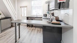 A modern kitchen with a central island, a built-in oven, and a window with a city view. - Liverpool Harrow Road Sleeps 6- Infinity Apartment (Liverpool)