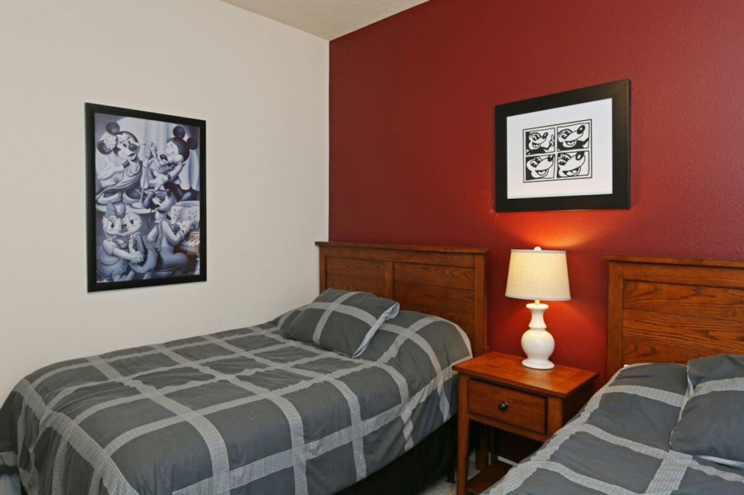 Habitación de hotel con dos camas, una mesita de noche con lámpara y dos cuadros enmarcados en la pared.