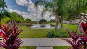 A landscaped garden with a pond, palm trees, and a pathway. - Your VIP Home in Orlando - Disney 25106 (Kissimmee)