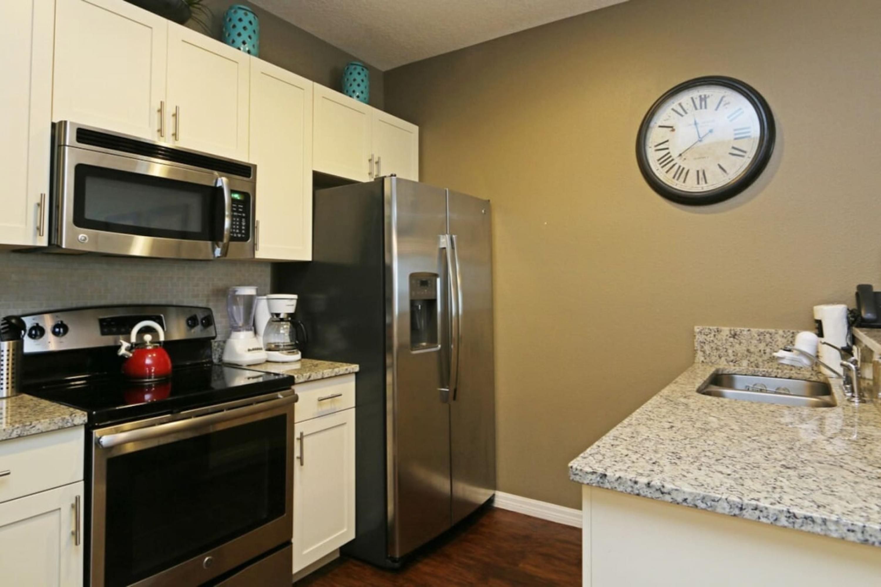 A kitchen with stainless steel appliances, a microwave, a refrigerator, and a clock on the wall.